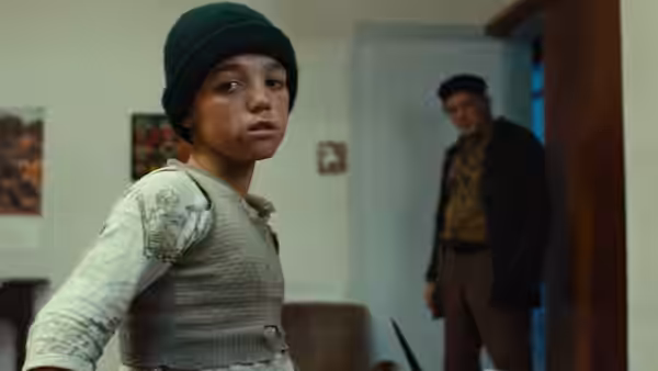 A boy in a green beanie looks back at a man in the doorway