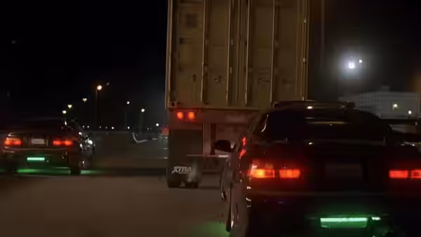 Two cars speed after a truck along a dark highway at night