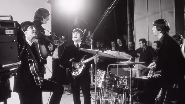 The Beatles perform with guitars and drums on a television studio set