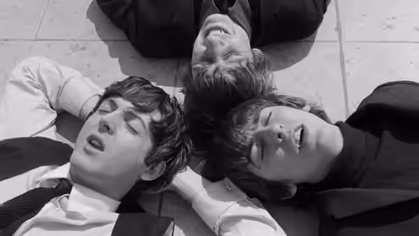 Three young men lie on a tiled floor with their heads together