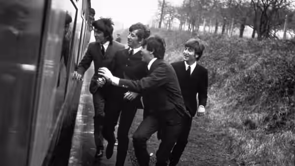 The Beatles crowd around an open train doorway beside a country platform