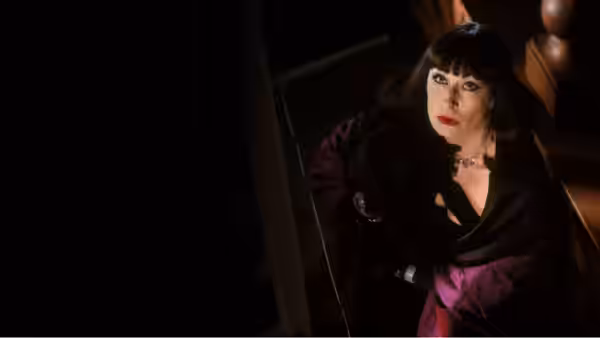 Miss Eva Ernst (Anjelica Huston) looks up from a dimly lit stairwell