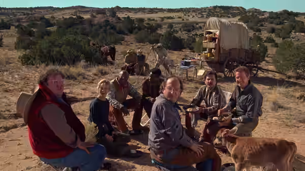 Mitch Robbins and companions seated on the ground near a covered wagon