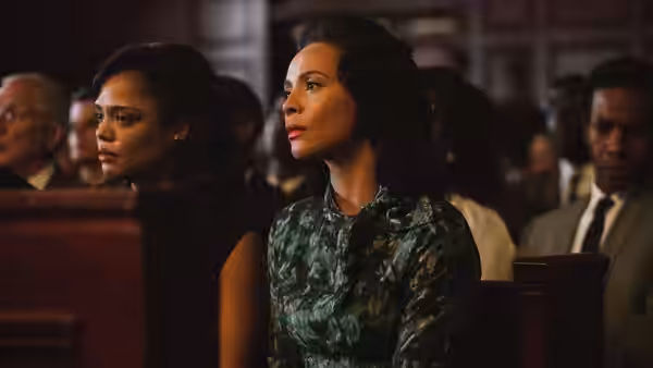 Coretta Scott King (Carmen Ejogo) seated in a church pew beside another woman