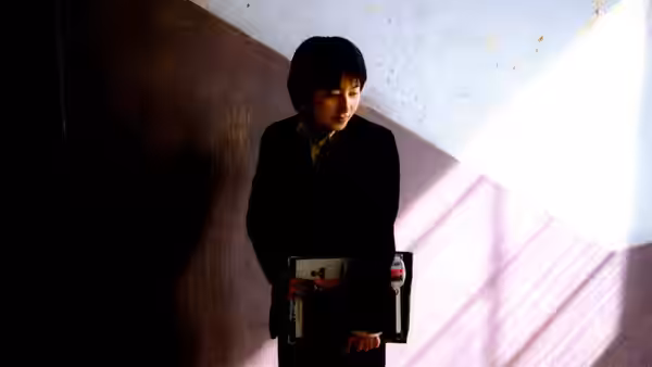 A woman in dark clothes holds a box in a brightly lit hallway