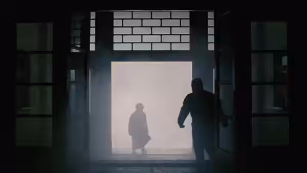 Two figures meet at a bright doorway inside a shadowy building