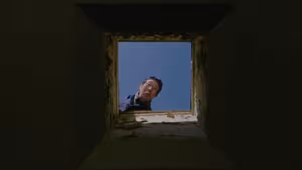 A man leans over an opening and looks down from above