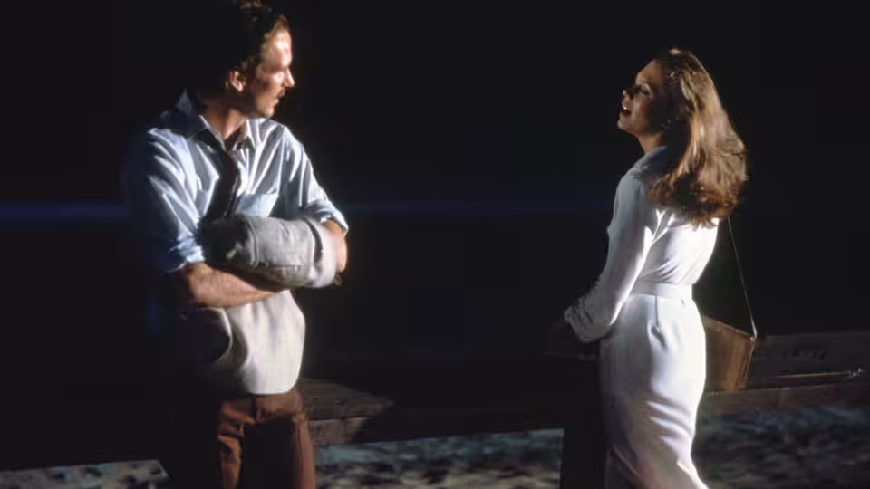 Ned Racine (William Hurt) with arm in cast faces Matty Walker (Kathleen Turner) on a dock at night