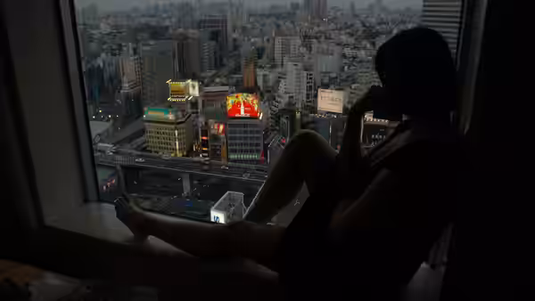 A woman sitting on a windowsill overlooking the illuminated city at night