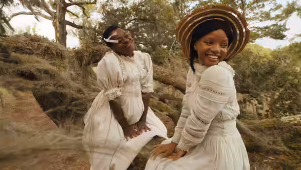 Two young women in white dresses smile together among trees and rocks