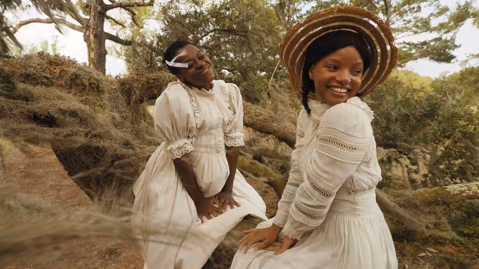 Two young women in white dresses smile together among trees and rocks