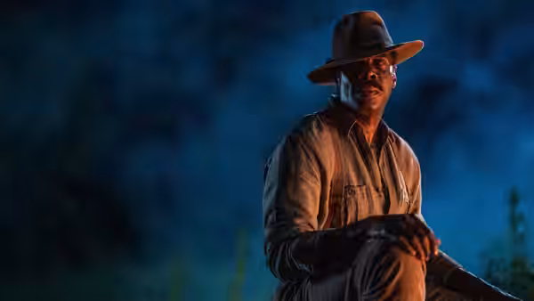 Mister (Colman Domingo) sits outdoors at night beneath a wide-brimmed hat