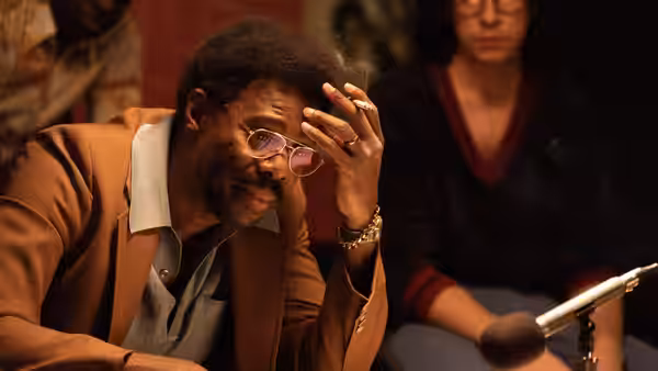 a man with glasses and an afro smoking a cigarette in a dim room