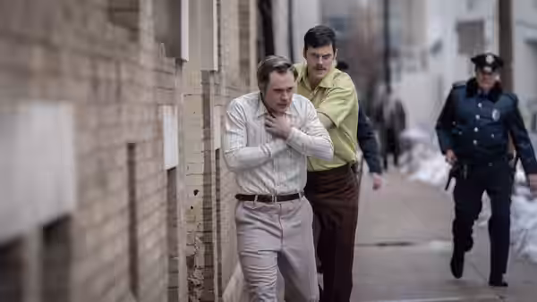 Tony Kiritsis (Bill Skarsgård) held by Richard Hall (Dacre Montgomery) against a brick wall