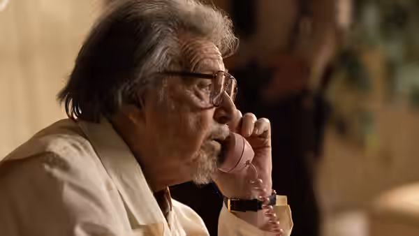 an older man with glasses speaking on a pink telephone indoors