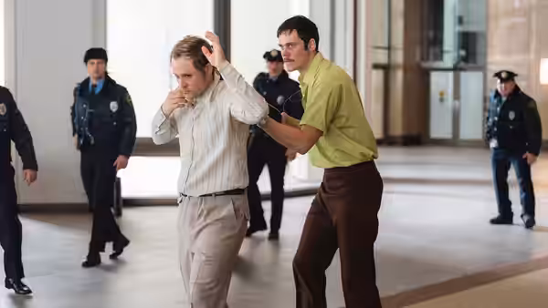 Tony Kiritsis (Bill Skarsgård) held by Richard Hall (Dacre Montgomery) inside a lobby with police