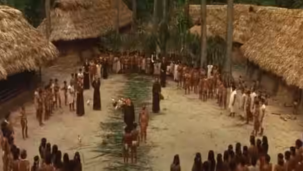A large circle of villagers gathers around robed figures in a jungle clearing