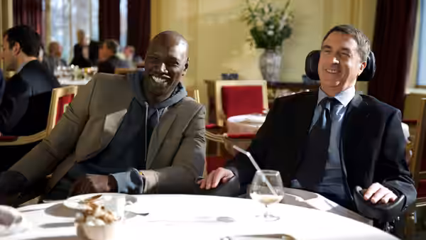 Driss (Omar Sy) and Philippe (François Cluzet) smiling at a restaurant table