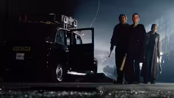 Three people standing beside an open black taxi at night