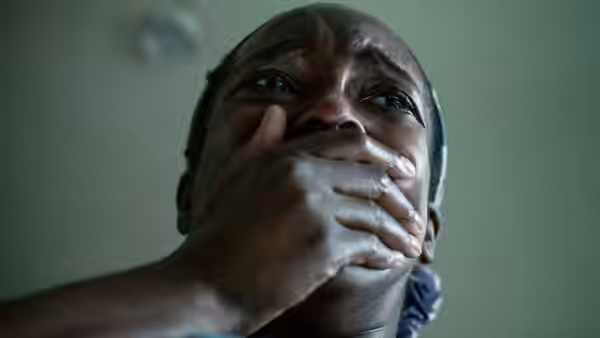 Bol Majur (Sope Dirisu) covers his mouth with one hand indoors