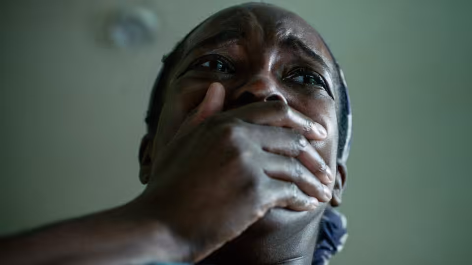 Bol Majur (Sope Dirisu) covers his mouth with one hand indoors