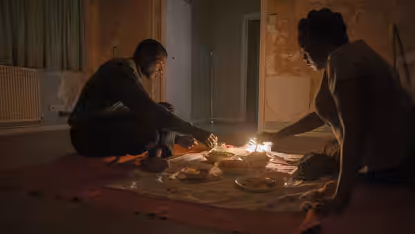 Bol and Rial kneel over food and candles spread on a blanket