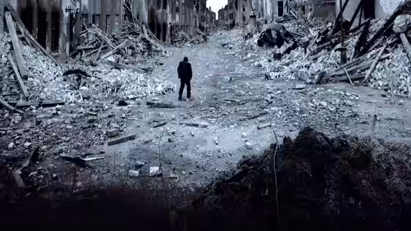 A lone figure walking through a wide street of collapsed buildings