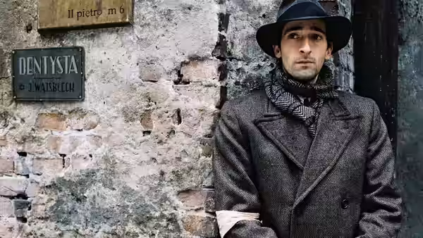 Władysław Szpilman (Adrien Brody) in hat and coat beside brick wall