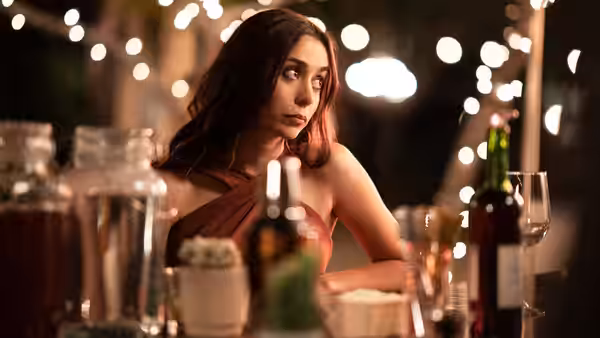 Tala (Camila Mendes) sits at a wedding reception table beneath string lights