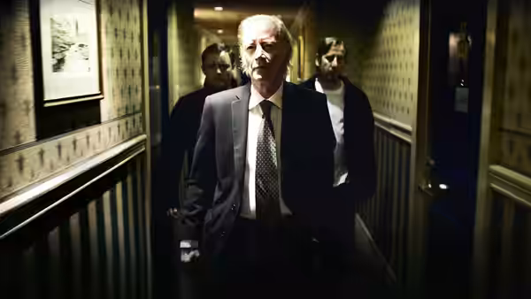 The Client (Struan Rodger) walks ahead down dim hallway