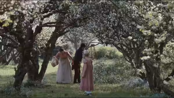 Two women stand beneath flowering trees in an orchard, one carrying a basket