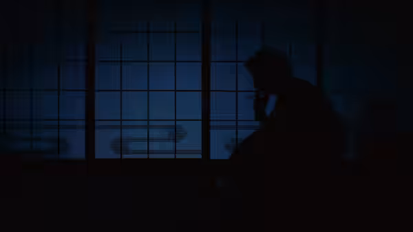 A man sits in silhouette beside a window, holding a phone to his ear