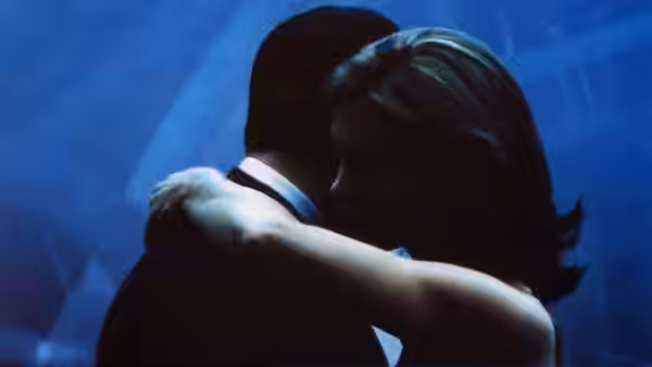 A man and woman embrace in a dim, blue-lit room