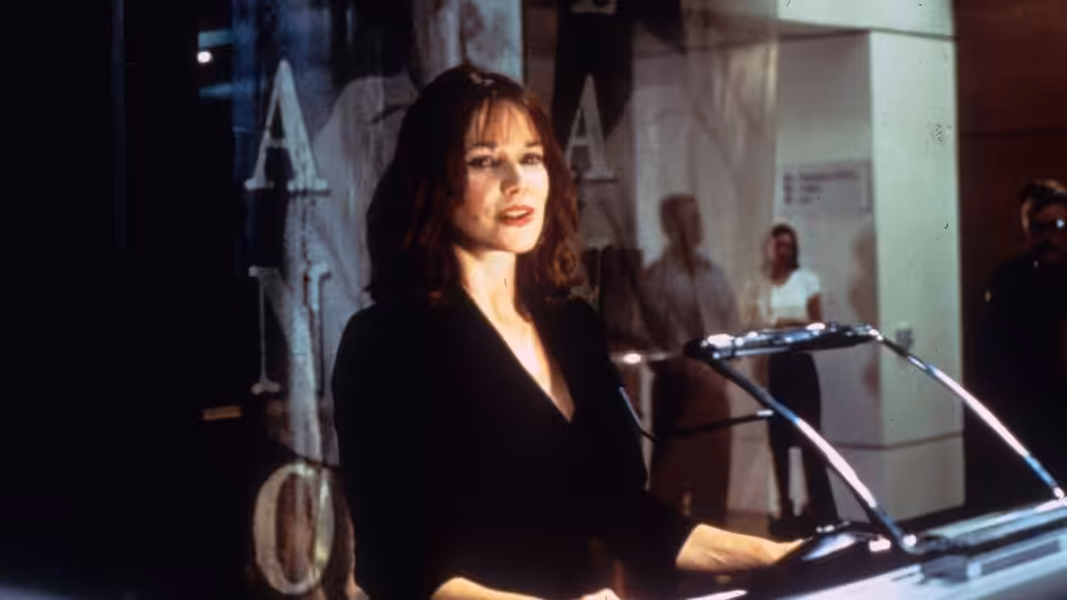 A woman stands at a lectern inside a public building