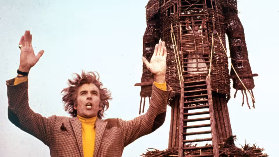 Sergeant Neil Howie (Edward Woodward) raises his arms before the wicker man