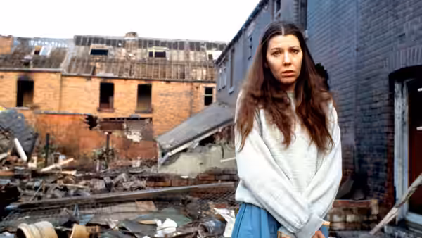 A woman standing with arms crossed among rubble of ruined brick buildings