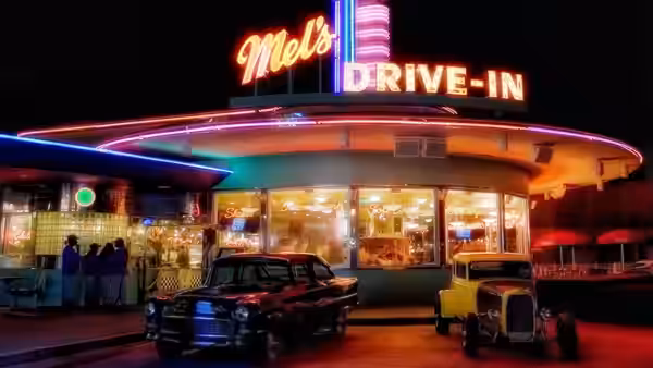 classic cars parked in front of a brightly lit drive-in restaurant at night
