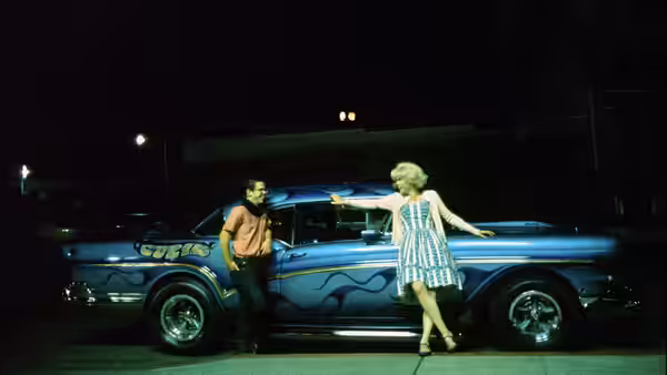 a man and woman stand beside a blue flame-painted car at night