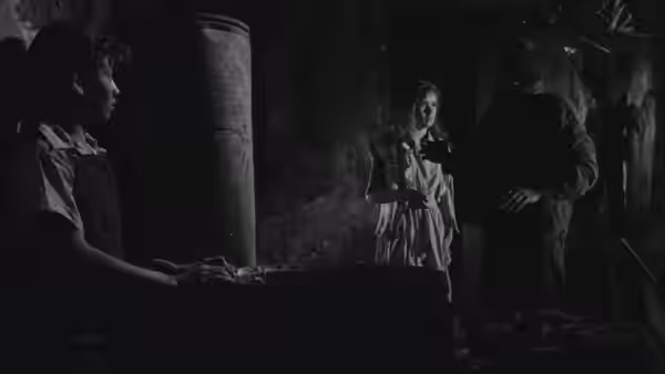 Man gesturing toward a girl as a boy watches in a dim room