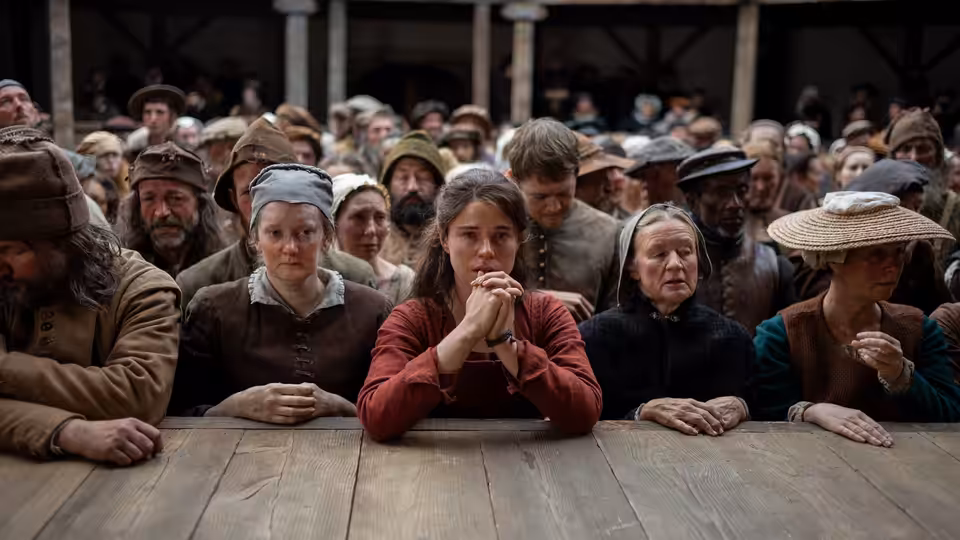 a group of people in period clothing stand behind a wooden table