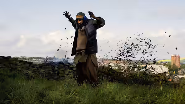 Omar (Riz Ahmed) on a hill with arms raised among flying birds