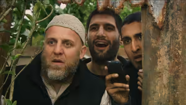 Three men peering from behind a rusted post, one holding a phone
