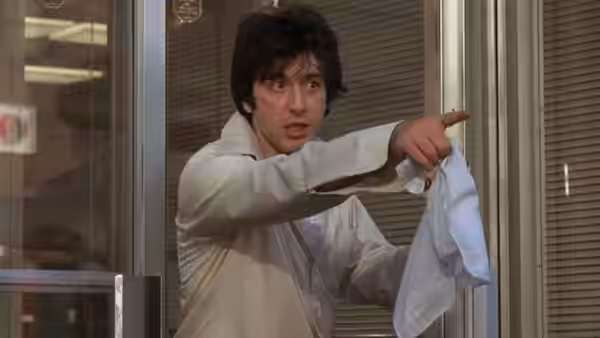 Sonny (Al Pacino) in a white shirt points out from a doorway holding cloth