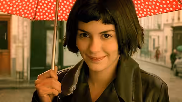 Amélie (Audrey Tautou) smiles under a red polka dot umbrella on a street