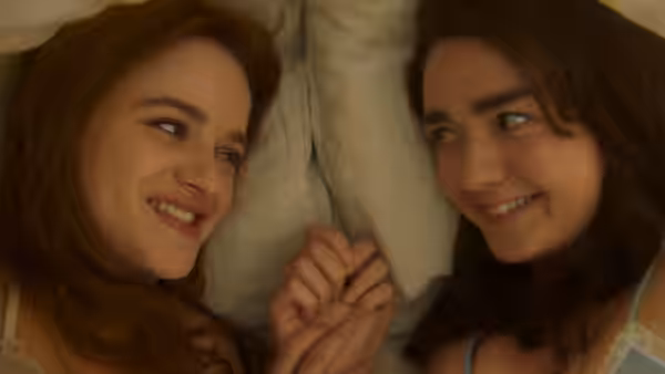 Two young women lying in bed smiling and holding hands