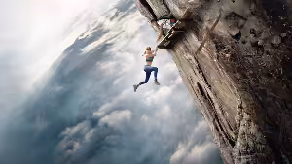 A climber scales a sheer cliff high above the clouds as another watches