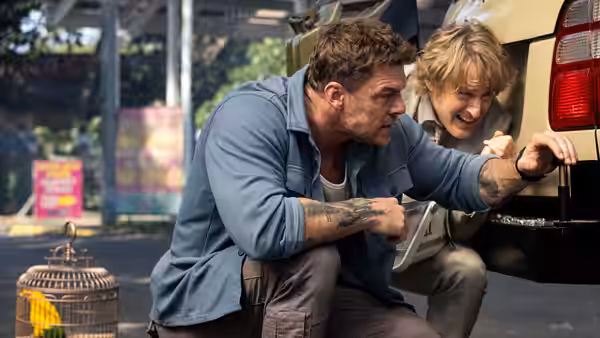 Hank Malone (Alan Ritchson) and Ben (Owen Wilson) crouching by a car