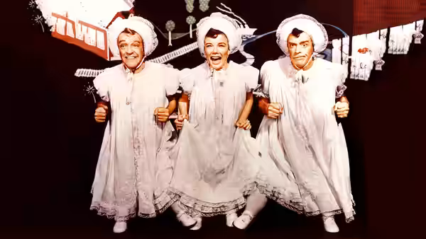 Three male performers in matching white dresses and bonnets dance in a line