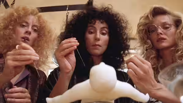 Jane Spofford (Susan Sarandon), Alexandra Medford (Cher) and Sukie Ridgemont (Michelle Pfeiffer) examine a small white figure
