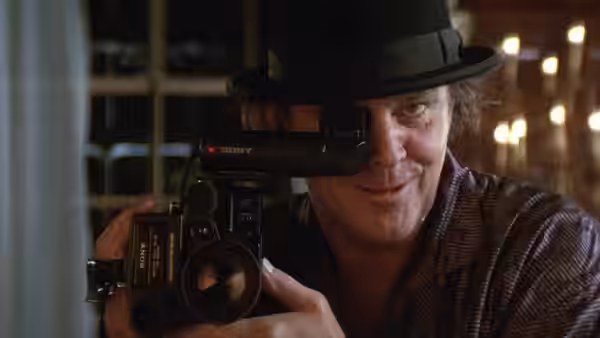 Daryl Van Horne (Jack Nicholson) peers through a camcorder while wearing a dark hat